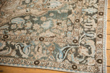 Distressed Baktiari carpet corner showing faded dusty teal, ivory palmettes, and vinery.