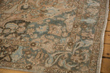 Distressed Baktiari carpet corner with even wear, featuring muted floral vinery and geometric border.