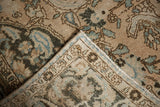 Folded corner of the distressed Baktiari rug, revealing faded blue floral motifs and foundation.