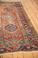 Worn brick red field, navy geometric border, and beige fringe on vintage Heriz runner.
