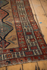 Antique Serab runner corner showing intricate geometric red and blue borders on a worn camel field.