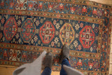 Vintage Malayer runner showing repeating geometric guls and starburst motifs in navy blue, red, gold.