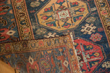 Vintage Malayer runner corner folded, showing navy, red, gold geometric guls and textured wear.