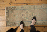 Faded ivory and pale green distressed Oushak runner with geometric diamond medallion.
