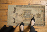 Distressed Oushak rug's geometric medallion, stylized florals, in muted ivory, beige, and soft green.