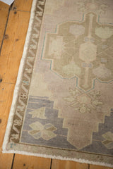 Distressed Oushak rug corner with mauve, beige, and pale blue geometric pattern, even wear.
