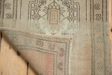 Curled corner of vintage Oushak rug mat, showing secured selvage and distressed low pile.