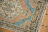 Distressed Oushak rug corner texture with pale terra cotta and blue geometric border, visible fringe.