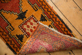 Distressed Oushak rug corner showing worn orange geometric pile, fringe, and striped back.
