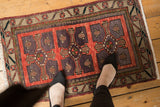 Distressed vintage Oushak rug corner with brick red field, dark violet motifs, and ornate floral border.