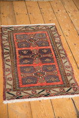 Distressed Oushak rug corner: brick red, violet patterns, sage floral border, and fringe.