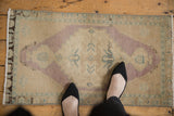Distressed Oushak rug mat corner, showing dusty mauve medallion, ocean green spandrel, and even wear.