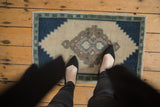 Distressed vintage Oushak rug displaying ivory field, mauve and green diamond medallion, navy spandrels.