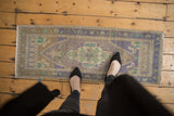 Distressed Oushak runner with elongated medallion featuring muted mauve, lilac, and mint tones.