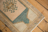 Distressed Oushak rug corner showing beige border, faded blue-green, and white fringe.