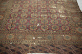Antique Turkmen carpet with intricate border designs, geometric patterns, and visible scattered holes.