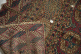 Antique Turkmen carpet's folded corner reveals geometric gul motifs, wear, and a visible hole.