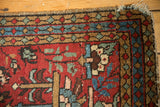 Heriz rug corner with cherry red field, sky blue geometric borders, and tattered fringe.