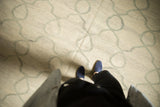 Kilim rug featuring ivory and pale slate grey Moroccan tile vines, with feet visible.
