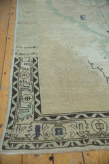 Vintage distressed Oushak rug corner with even wear, highlighting charcoal serrated border and stylized blossoms.