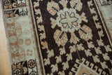 Distressed Oushak runner: dark chocolate floral field, ivory geometric border, and visible low pile.