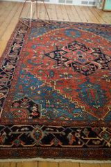 Antique Heriz carpet showing madder red field, bold geometric patterns, and intricate navy blue border.