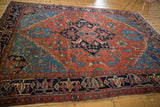 Antique Heriz carpet's navy geometric border, madder red field with stylized plant motifs.