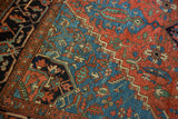 Geometric Heriz pattern in madder red, sapphire blue, and mallard green with visible pile wear.