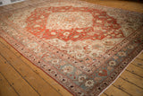 Angled view of a distressed Khoy carpet's slate blue border and brick red floral field.