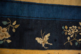 Pictorial bird motif and floral sprays on the worn indigo border of a vintage Chinese rug.