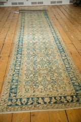 Distressed Hamadan runner end, showing beige field, blue floral border, and secured fringe.