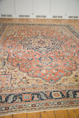 Intricate navy border and delicate floral vinery on the antique Serapi rug's pale brick red field.