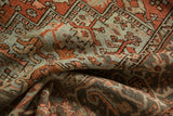 Distressed Heriz carpet showing geometric palmettes, dusty rust, muted blue, and softened pile.