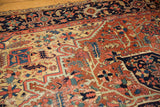 Antique Heriz carpet showcasing geometric vinery in brick red, navy, and saffron, with visible wear.