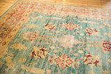 Distressed Turkish Oushak rug field showing abrashes, sky blue, blush coral, and ivory floral patterns.