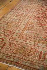 Distressed Joshegan rug corner with soft cinnabar, blue, ivory, and gold lattice design.
