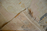 Vintage distressed Oushak rug corner with muted pile, tattered fringe, and hand-knotted foundation.