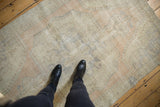 Feet on distressed vintage Oushak rug, highlighting worn texture and faded beige tones.