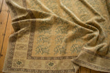 Textured distressed Oushak rug: pale gold field, blue-green florals, coffee brown border detail.