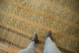 Distressed Oushak carpet's faded gold field, blue-green floral vine motifs, and patterned border.