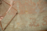 Distressed Oushak carpet with worn pale peach and ivory pile featuring abstract motifs, under a copper stand.