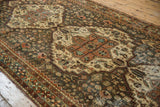 Distressed vintage Bakhtiari runner, its stylized pale terracotta medallion and dusty dark teal field.