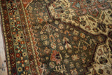 Distressed dark teal Bakhtiari rug with stylized terracotta, beige plant and animal motifs, visible wear.