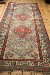 Persian Serab rug corner displaying madder red border, intricate germinating motifs, and worn pile.