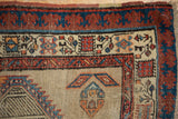 Vintage Serab rug corner with reciprocating madder red and indigo borders, beige field.