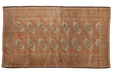 Distressed vintage Belouch rug with terra cotta guls, muted bronze, and halved medallions.