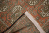 Folded vintage distressed Belouch rug corner, revealing terra cotta, bronze, silver pattern, and woven backing.