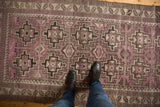Distressed vintage Belouch runner showing low pile, geometric medallions, and mottled purple, charcoal, and ivory hues.