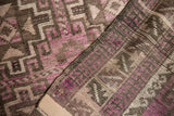 Distressed texture of vintage Belouch rug with geometric patterns in purple, charcoal, and ivory.