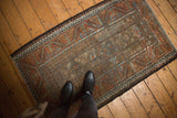 Distressed Belouch rug corner, coffee brown field with madder red guls and meandering vine border.